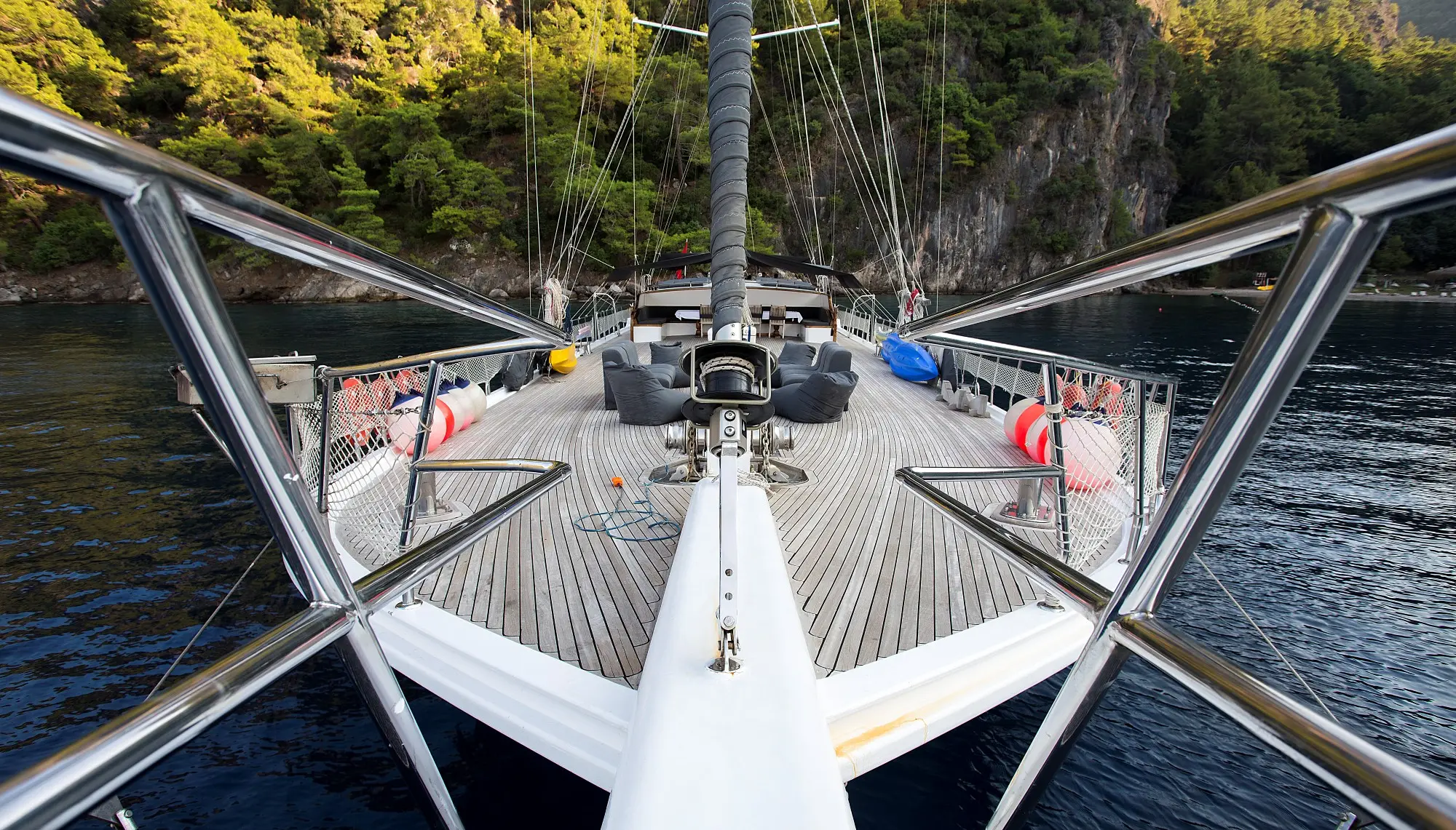 The deck of a sailing yacht facing a wooded shoreline